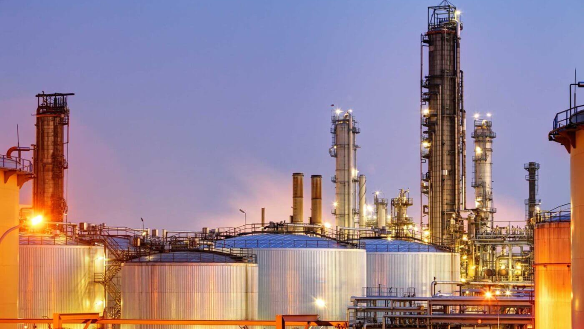 Large industrial facility with storage tanks and refinery towers illuminated at dusk