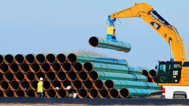 Excavator lifting steel pipes at a construction site
